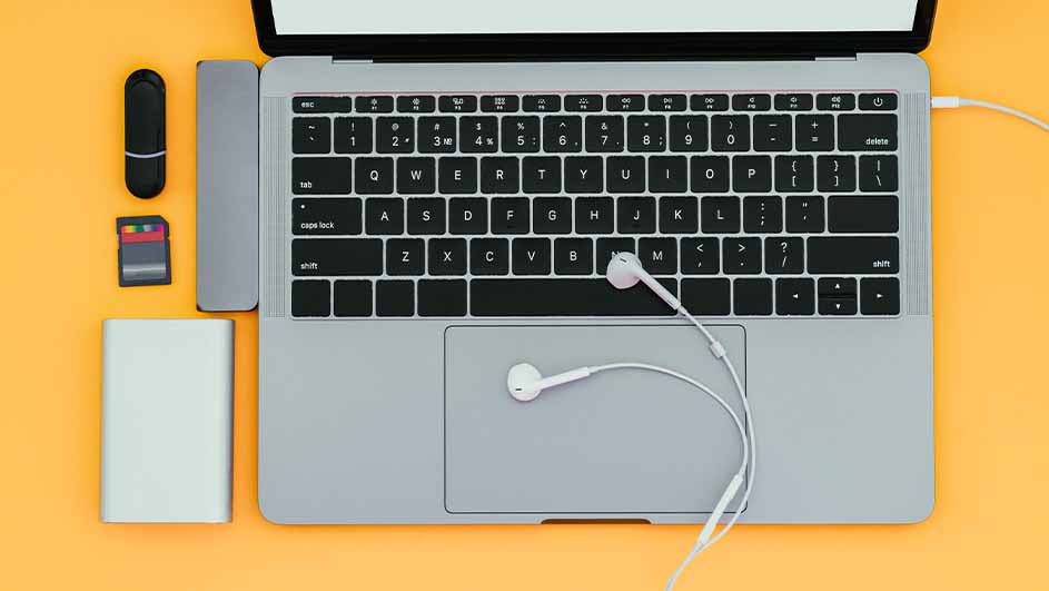 Laptop met oortjes, USB-stick, SD-kaart en powerbank op een gele achtergrond.