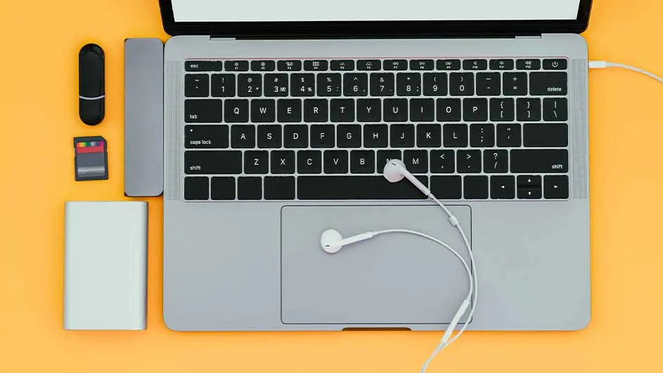 Laptop met oortjes, USB-stick, SD-kaart en powerbank op een gele achtergrond.