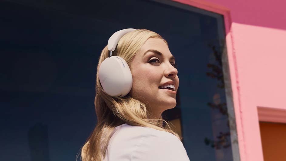 Een vrouw met een witte shirt en witte hoofdtelefoon glimlacht tegen een achtergrond van een blauwe muur en een roze deur.