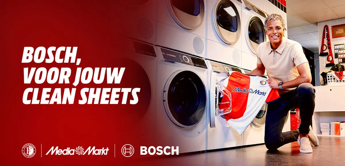 Giovanni van Bronckhorst gehurkt bij een wasmachine met een Feyenoord-shirt in zijn hand.