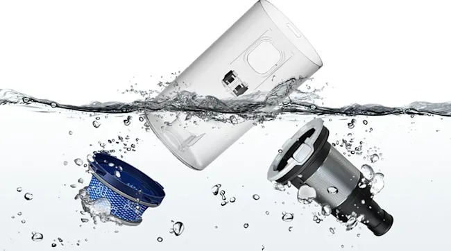 Een blauw filter, transparant stofreservoir en zwart-grijs onderdeel van een stofzuiger zweven los in helder water, met luchtbellen rondom.