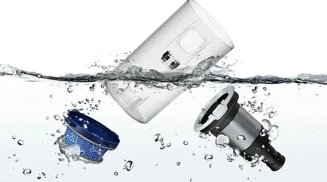 Een blauw filter, transparant stofreservoir en zwart-grijs onderdeel van een stofzuiger zweven los in helder water, met luchtbellen rondom.