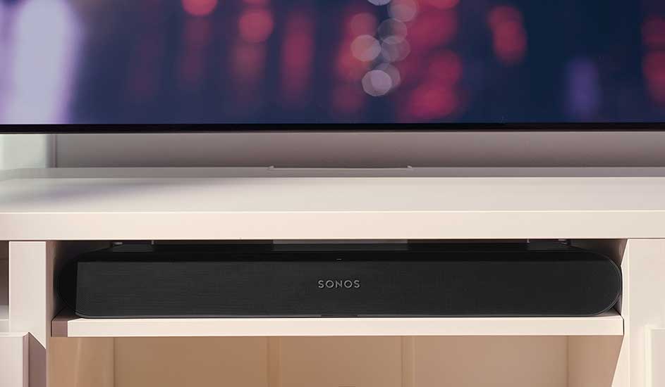 A black Sonos soundbar sits neatly beneath a television on a white media shelf, creating a clean and modern interior look.