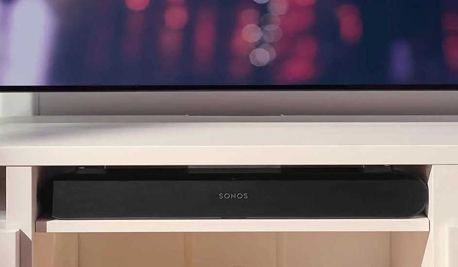 A black Sonos soundbar sits neatly beneath a television on a white media shelf, creating a clean and modern interior look.