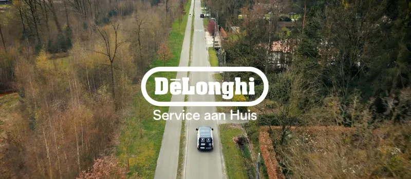 Een lange weg met een auto, omgeven door bomen en het DeLonghi logo met "Service aan Huis" in het midden.