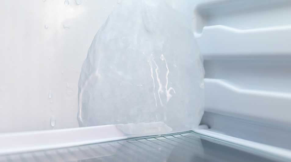 Dikke ijsbult groeit tegen de achterwand van een vriesvak, met glanzend bevroren oppervlak en druppels die erboven langs lopen.
