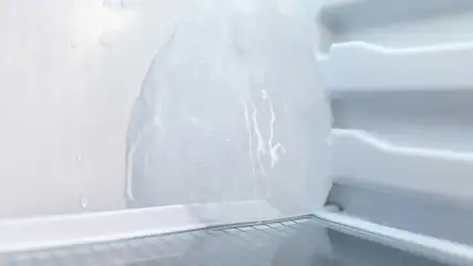 Dikke ijsbult groeit tegen de achterwand van een vriesvak, met glanzend bevroren oppervlak en druppels die erboven langs lopen.