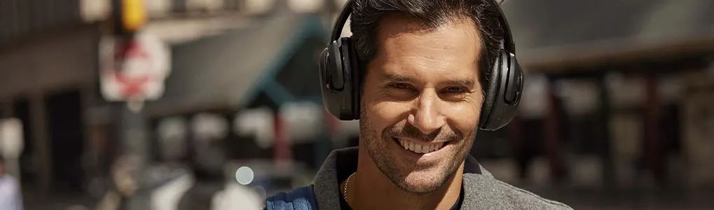 A person wears headphones and a gray jacket outside. Background includes traffic lights and blurred buildings.