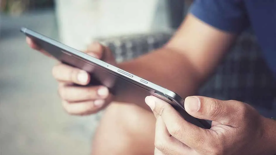 Een persoon houdt een donkergrijze tablet vast met beide handen, de zijkant van het apparaat is zichtbaar.