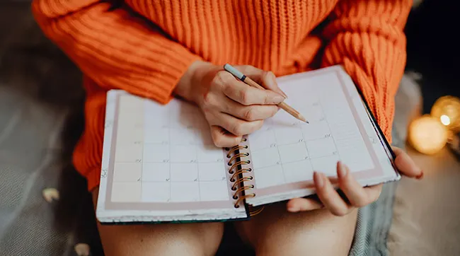 Handen schrijven met potlood in een open maandplanner.