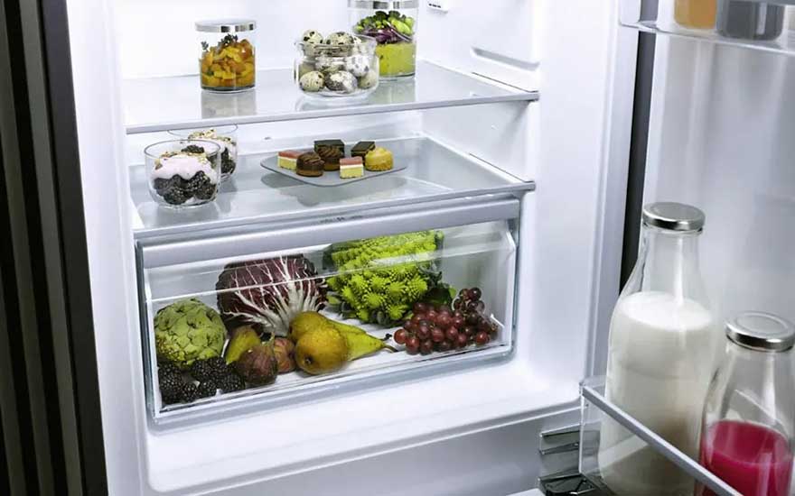 Open koelkast netjes gevuld met verschillende verse groenten, fruit, zuivel en desserts. Alles lijkt op orde en schoon.