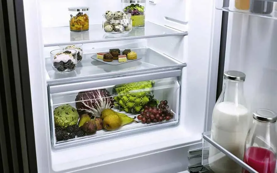 Open koelkast netjes gevuld met verschillende verse groenten, fruit, zuivel en desserts. Alles lijkt op orde en schoon.