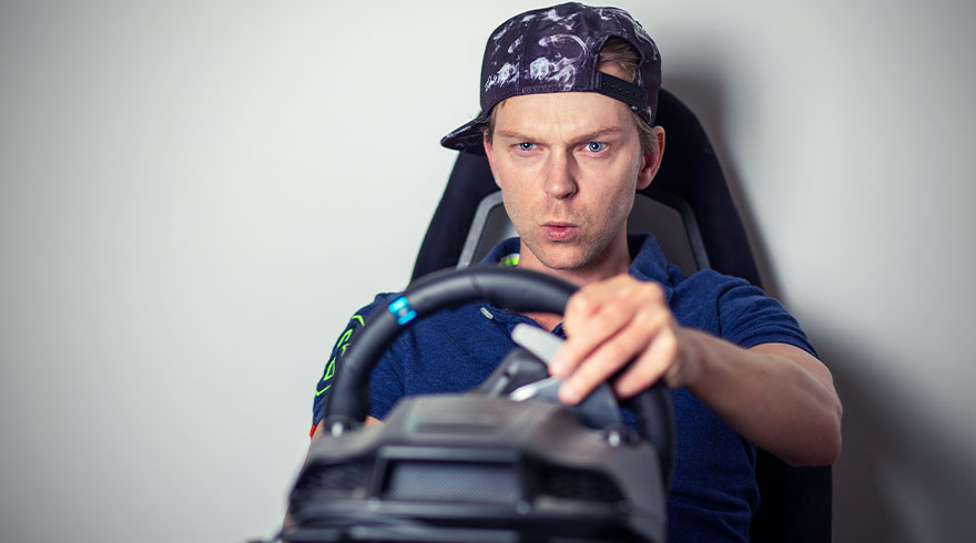 Een man met een pet zit in een zwarte stoel achter een zwart stuur met blauwe en groene details.