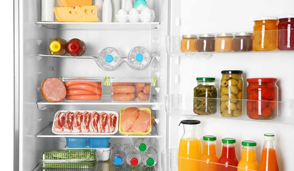 In de koelkast liggen kaas, eieren, worsten, vlees, groenten, waterflessen, sappen, en in de deur staan potjes met olijven en augurken.