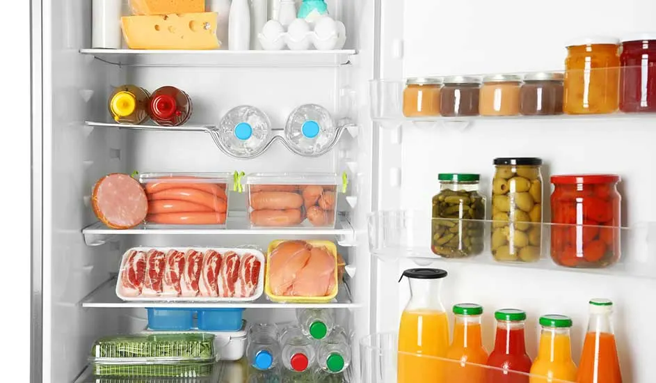 In de koelkast liggen kaas, eieren, worsten, vlees, groenten, waterflessen, sappen, en in de deur staan potjes met olijven en augurken.