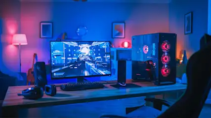 Een computeropstelling met een monitor waarop een game te zien is, een toetsenbord, speakers en een gaming pc met rode verlichting.
