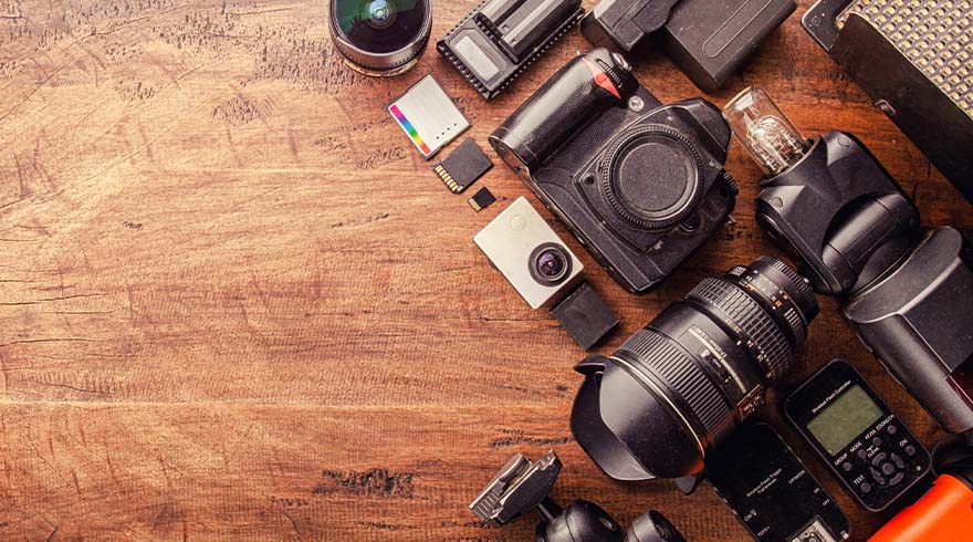Diverse zwarte camera-apparatuur, inclusief lenzen, flitsers en batterijen, liggen op een houten tafel.
