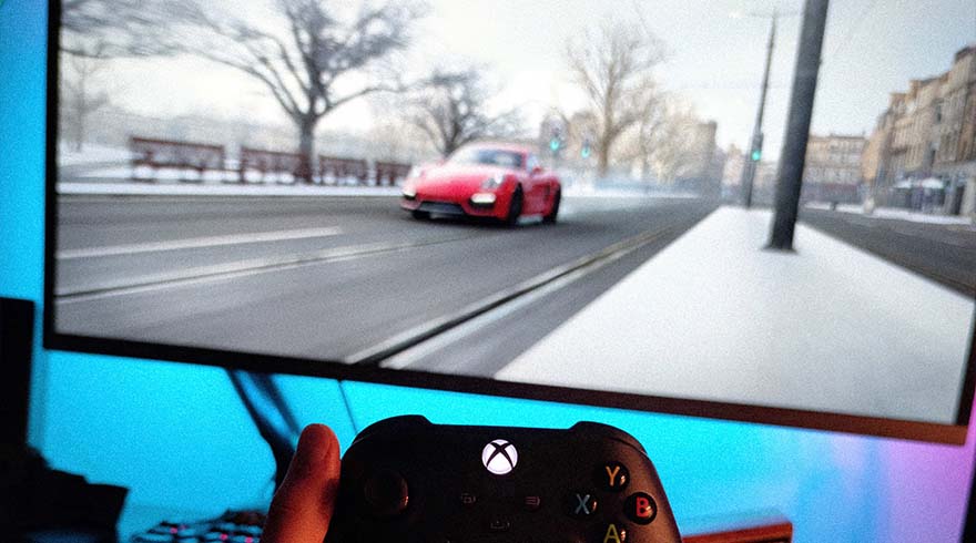 Een Xbox-controller in de hand voor een scherm waarop een rode auto op een besneeuwde weg rijdt.