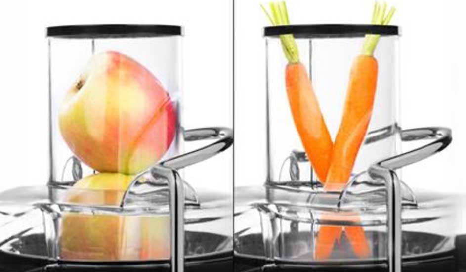 Op de afbeelding zie je een sapcentrifuge van Philips met links een appel en rechts twee wortels in de vulopening, klaar om geperst te worden.