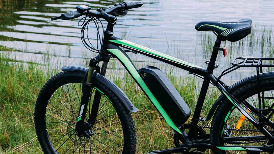 Een zwarte e-bike met groene accenten staat in gras, met water op de achtergrond.