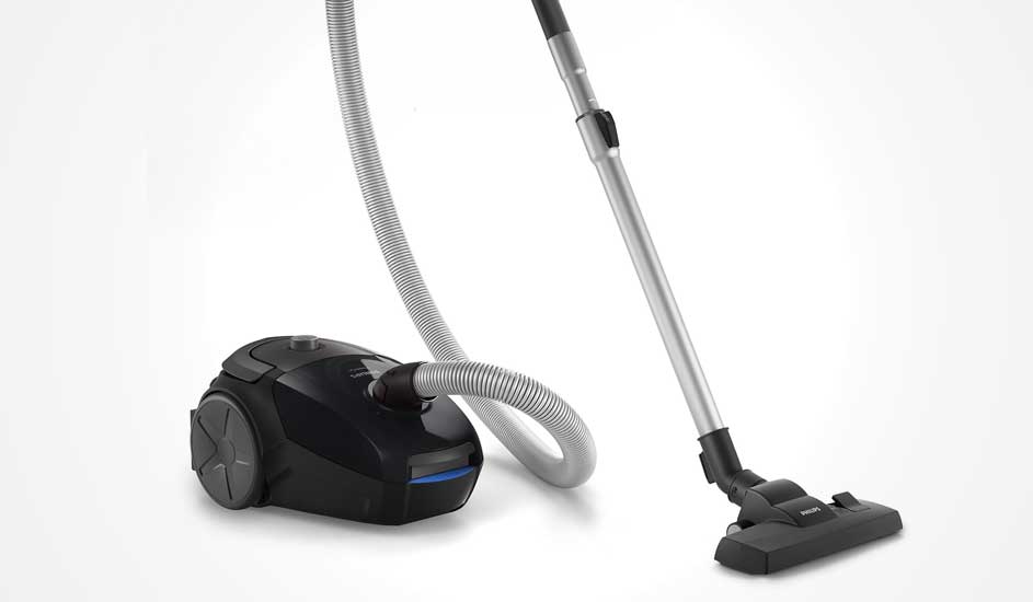 A compact black cylinder vacuum with silver tube and flexible hose is shown alone against a clean, bright white background.