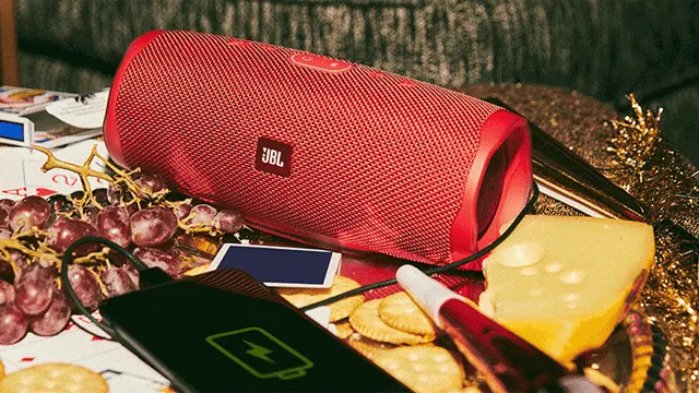 Rode JBL-speaker, druiven, kaas en een zwarte powerbank met een batterij-icoon op een tafel.