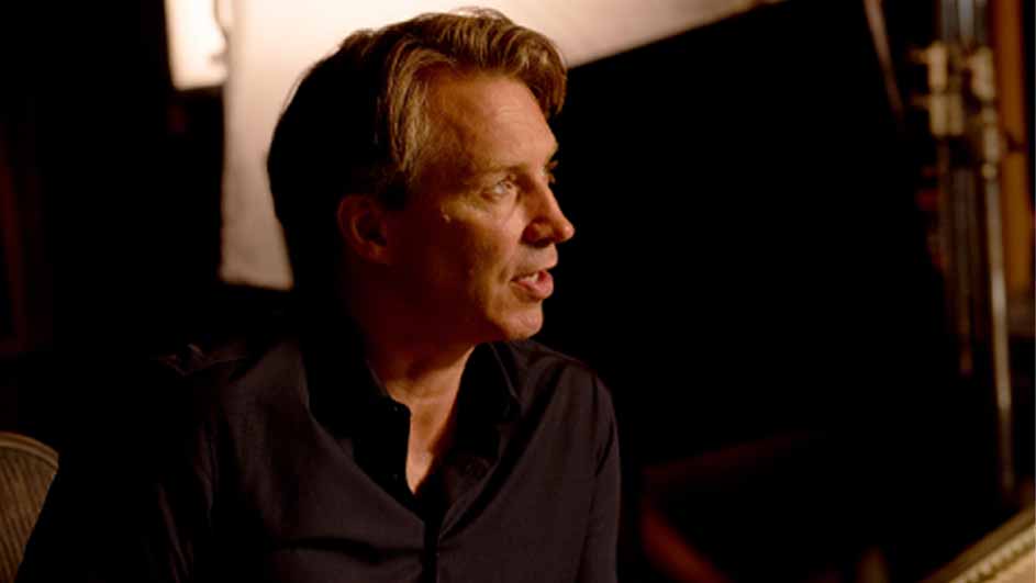 Een man in een zwart overhemd kijkt naar rechts, met lichte achtergrond elementen.