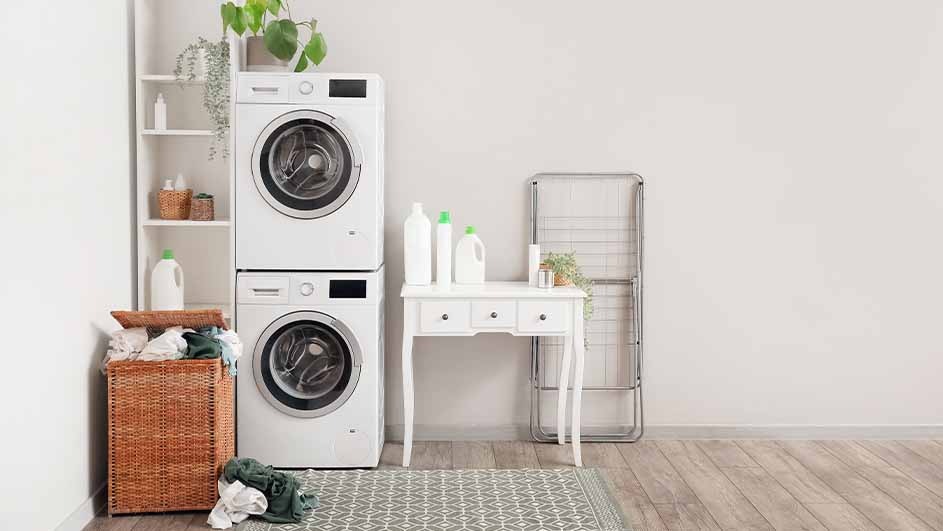 Laundry room with stacked white washer/dryer, wicker basket, white shelf, table, and folding rack on a patterned rug.