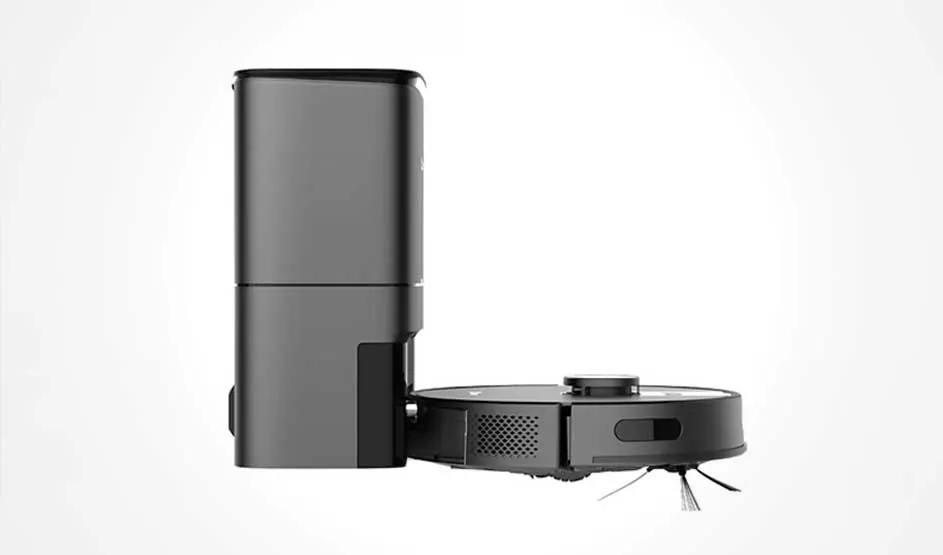 Een zwarte robotstofzuiger staat zijwaarts naast een hoog basisstation; je ziet ventilatieroosters, zijborstels en de verhoogde sensor bovenop.