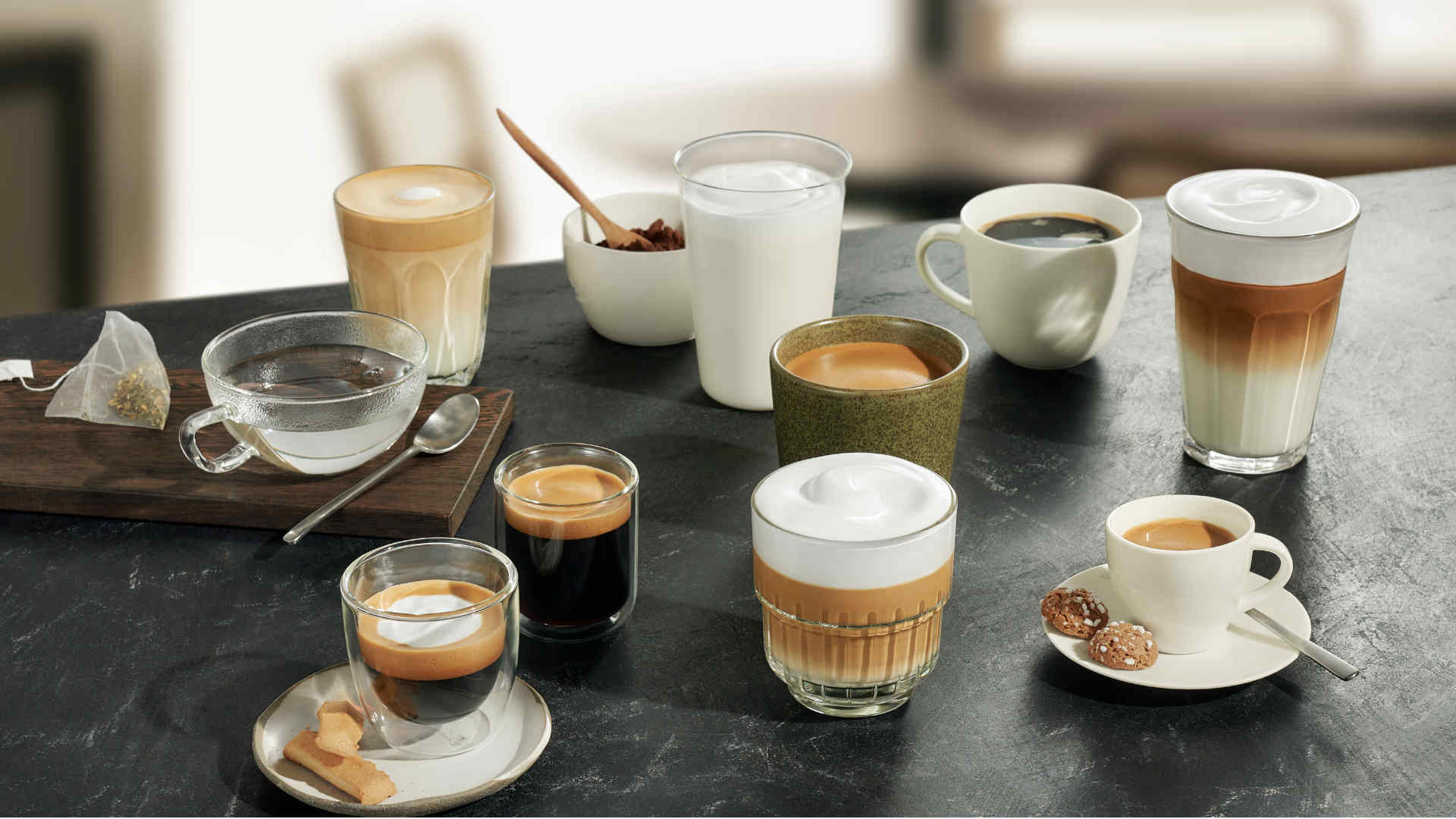 Diverse warme dranken op een donker oppervlak, waaronder thee, espresso, latte en koffie, in glazen en mokken.