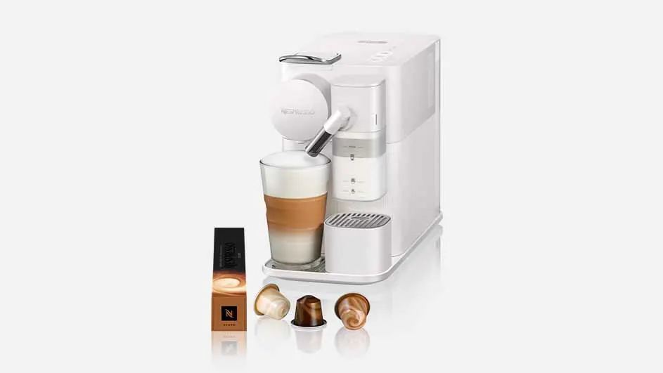 Een witte Nespresso-machine met een glas latte macchiato, capsuleverpakking en drie capsules op een wit oppervlak.