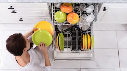 Een vrouw laadt een vaatwasser vol met borden, bekers en kommen in verschillende kleuren.