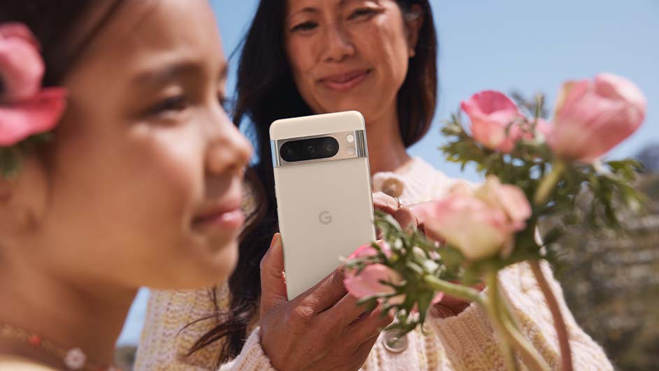 Een vrouw houdt een witte smartphone vast met bloemen op de voorgrond. Een meisje staat links met een bloem in het haar.