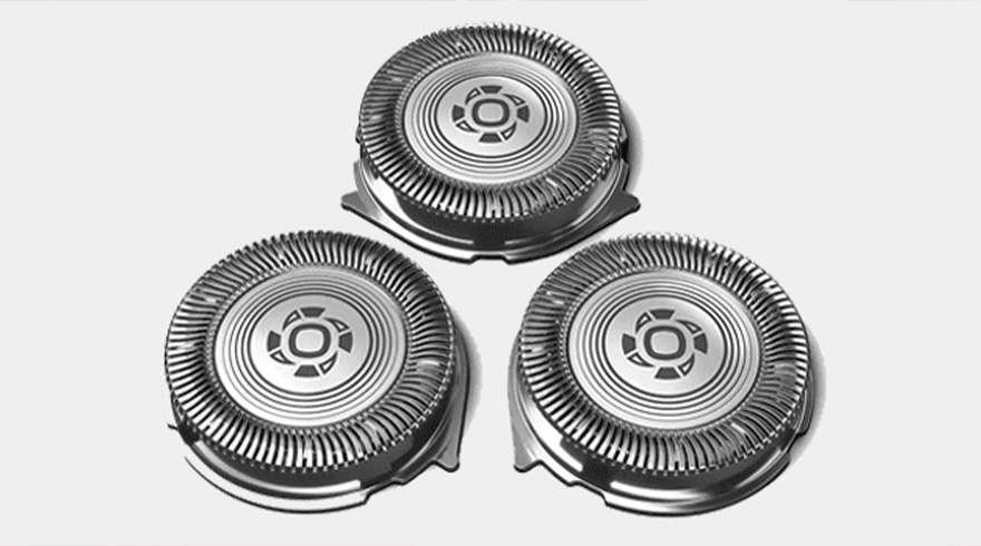 Drie zilverkleurige, ronde scheerkoppen op een witte achtergrond, elk met een patroon van cirkels en lijnen.