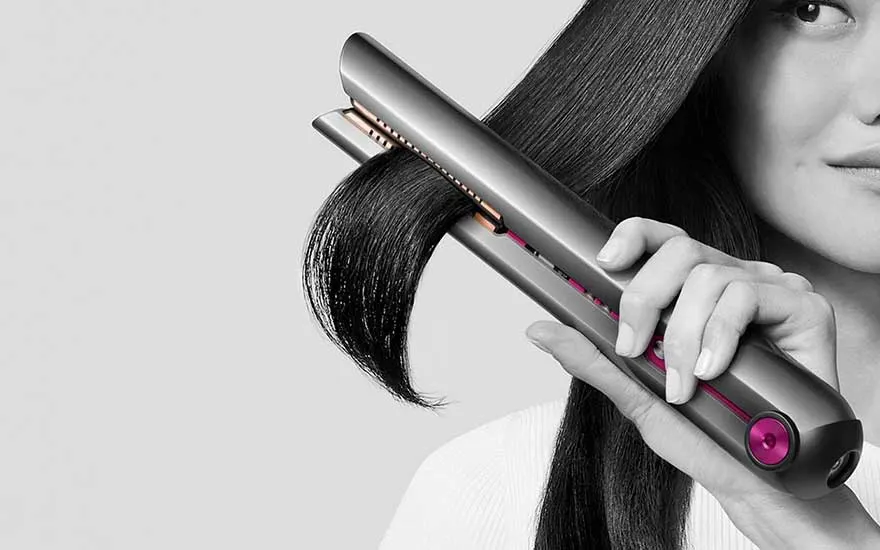 A model uses a modern straightener on glossy dark hair, as a section glides smoothly between the plates.
