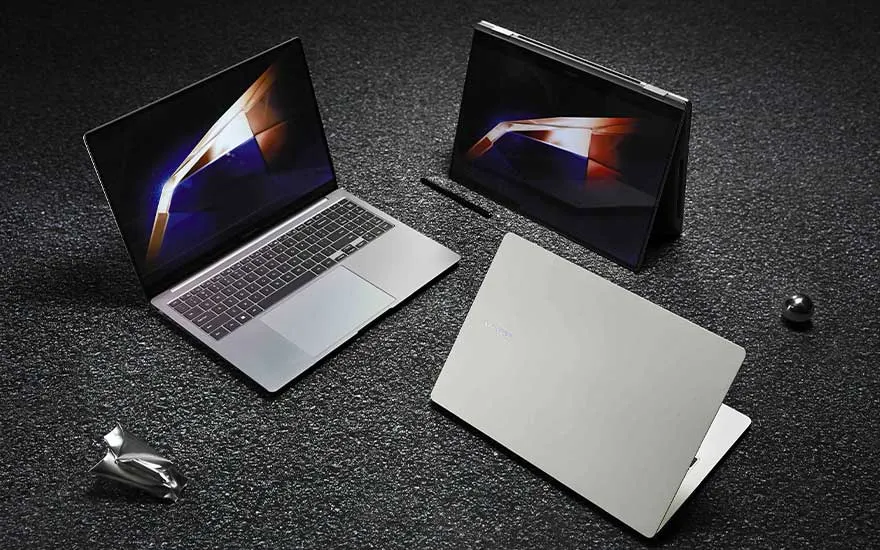 Drie slanke laptops staan op een donkere korrelige vloer; één open, één in tentmodus en één gesloten, met dynamische schermkleuren.