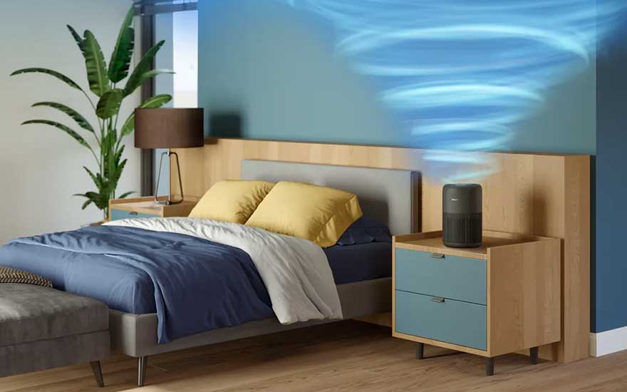 In a cosy bedroom, a compact air purifier on the bedside table forms a swirling blue vortex of clean air beside the neatly made bed.