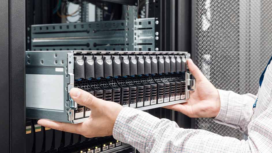 Een persoon in een wit overhemd plaatst een grijze server met zwarte harde schijven in een serverkast.