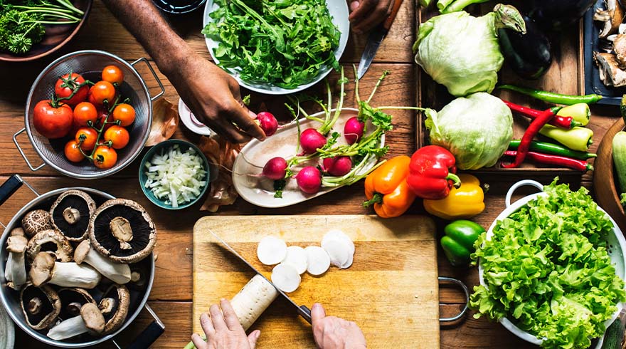 Een houten tafel met diverse groenten, waaronder tomaten, champignons, paprika's en sla, klaar voor bereiding.