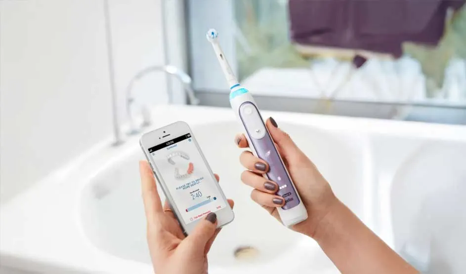 Handen houden een elektrische tandenborstel en smartphone met tandverzorgingsapp in een badkamer.