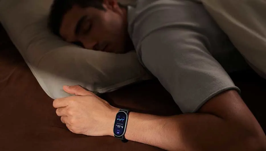 A sleeping person lies on a dark bed, wearing a smart fitness watch that gently tracks their nightly sleep cycles and patterns.