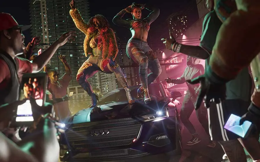 Nachtelijk straatfeest met mensen die filmen terwijl twee vrouwen dansen boven op een auto, omringd door stadslichten.