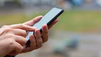 Een hand met een vinger op het scherm van een zwarte smartphone. Vage groene en grijze achtergrond.