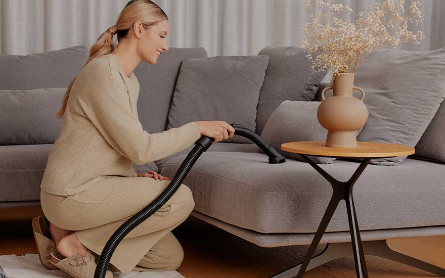 Een vrouw gebruikt een meubelborstel om de bank zorgvuldig schoon te maken, handig voor stof en haren.