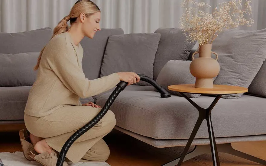 Een vrouw gebruikt een meubelborstel om de bank zorgvuldig schoon te maken, handig voor stof en haren.