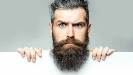 Een man met een lange baard houdt een wit bord vast tegen een grijze achtergrond.