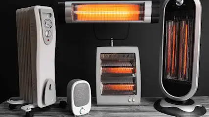 Verschillende elektrische kachels, waaronder modellen met olie, infrarood en ventilatoren, staan op een tafel tegen een donkere achtergrond.