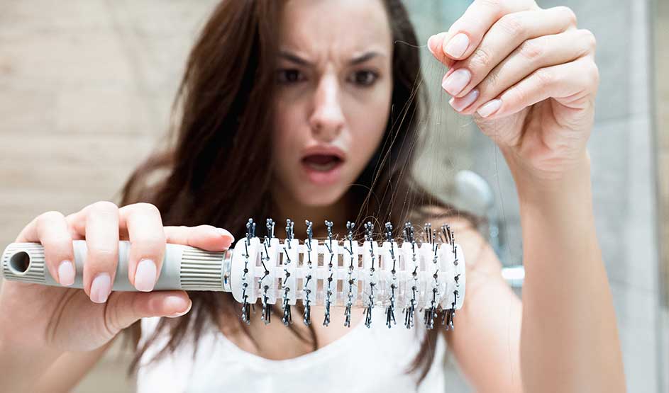 Persoon kijkt geschrokken naar haarverlies op een haarborstel in de badkamer.