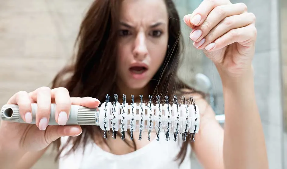 Persoon kijkt geschrokken naar haarverlies op een haarborstel in de badkamer.