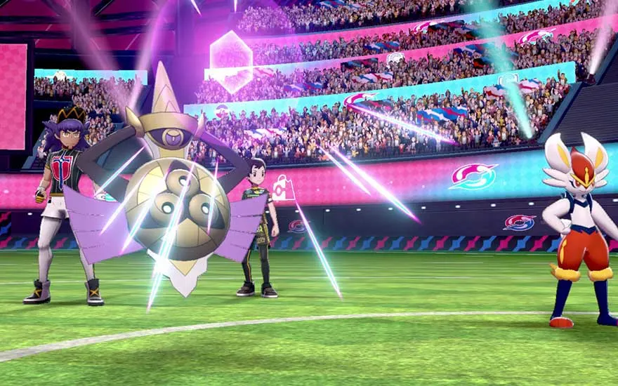 Inside a packed stadium, two Pokémon face off: a floating sword-and-shield and a fiery rabbit striker, as their trainers watch intently.